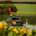 Voiture ouvreuse avec panneau "course cycliste" et drapeaux rouges